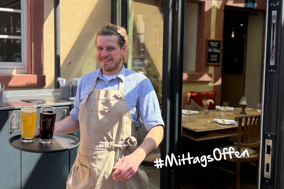 Kellner mit Tablett und zwei kühlen Getränken der gerade den Innenhof betritt für den Mittagstisch in Ettlingen: Watt’s Brasserie jetzt auch mittags geöffnet